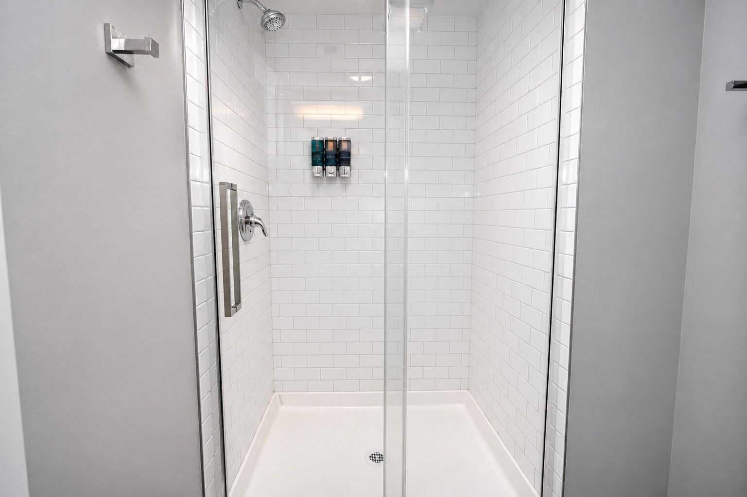 A modern shower with a glass door, white tiled walls, and a visible showerhead.