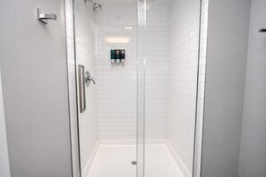 A modern shower with a glass door, white tiled walls, and a visible showerhead.