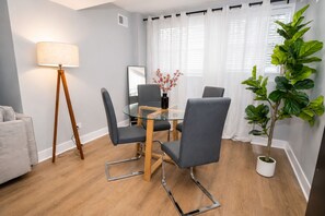 A modern dining area with a glass table, grey upholstered chairs, a floor lamp, and a potted plant.