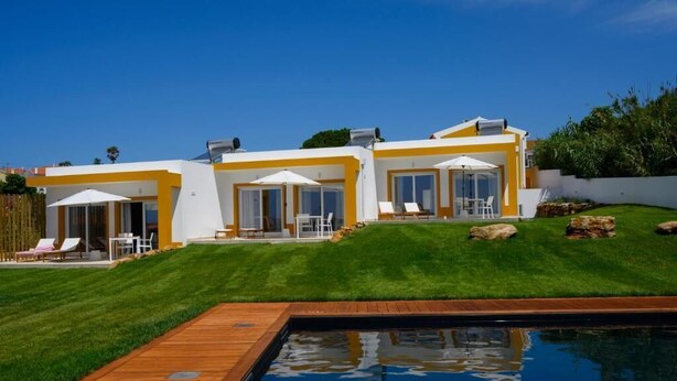 Een modern huis met een zwembad, een terras met lounge fauteuils en een verzorgd gazon.