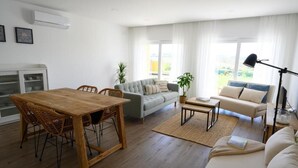 Een moderne woonkamer met een houten eettafel, een grijze bank en een beige zithoek.
