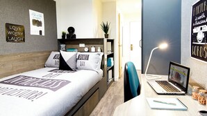 Ein modernes Schlafzimmer mit einem Bett, einem Schreibtisch mit Laptop, einem Stuhl und einer Tür zu einem anderen Raum.