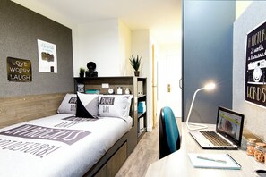 A modern bedroom with a bed, a desk with a laptop, a chair, and a door leading to another room. - Student Only Bentley House (Birmingham)