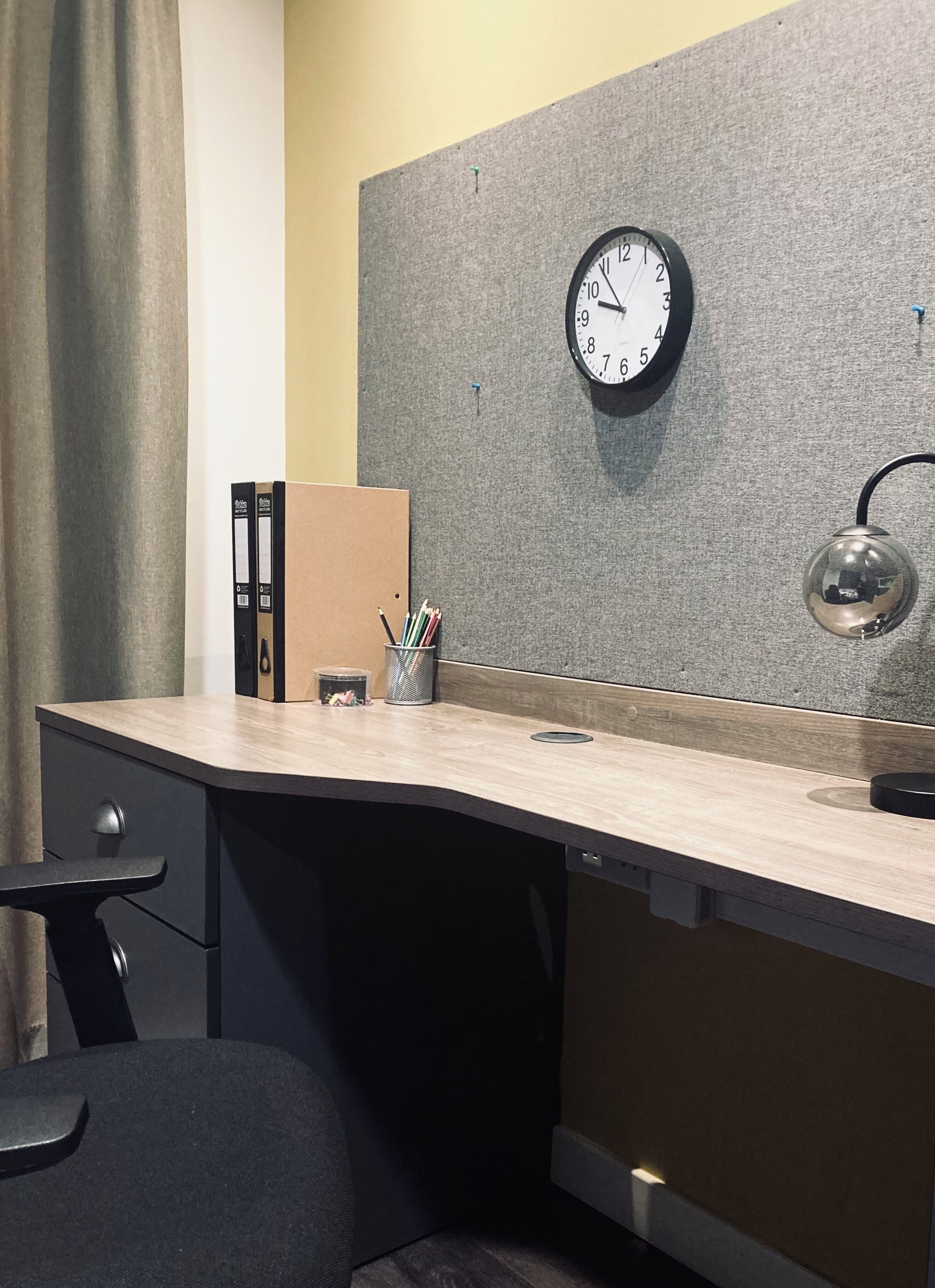 A modern office desk with a clock, a pencil holder, and a trash can.
