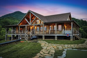 A lodge with a stone pathway, wooden deck, and a view of the forest. - New Listing, Hot Tub, Game Room, Relaxing Outdoor Space, Putting Green (Sevierville)