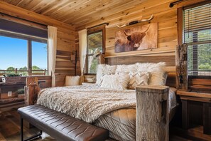 A wooden cabin bedroom with a large bed, a bench, and a window with a view. - New Listing, Hot Tub, Game Room, Relaxing Outdoor Space, Putting Green (Sevierville)