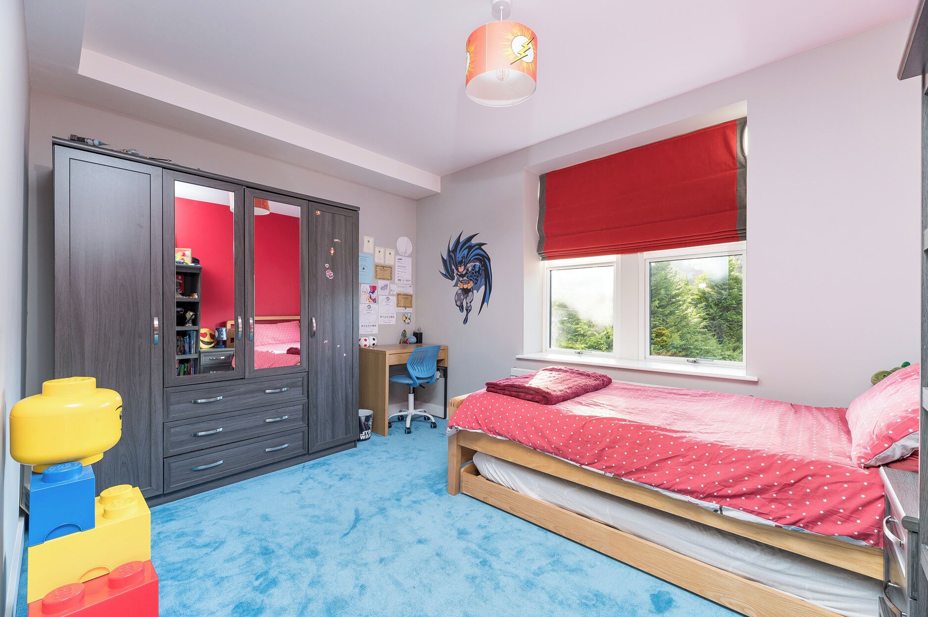A child's bedroom with a bed, wardrobe, desk, and toys.