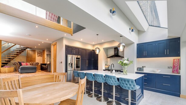 Una cocina moderna con una isla central, armarios azul oscuro y una escalera visible que sube a un nivel superior.