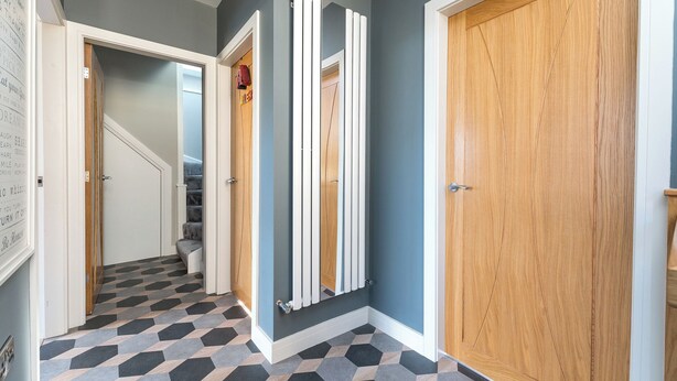 Un pasillo con suelo de diseño geométrico, una puerta de madera y un radiador blanco.
