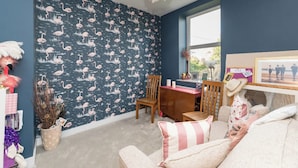 Una habitación con pared azul oscuro, papel tapiz estampado, una silla de madera, una mesita pequeña y un sofá con almohadas a rayas.