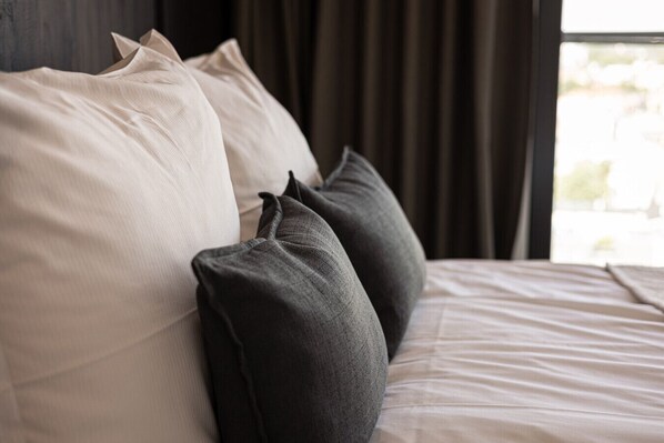 A bed with two pillows, a window with curtains, and a view of the outdoors.