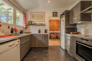 A modern kitchen with stainless steel appliances, a dishwasher, and a window with a view of trees. - Between the ocean and the Bassin, near the tip, house with large garden (Lège-Cap-Ferret)