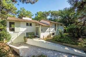 Uma casa de dois andares com telhado de telhas, entrada frontal e um pequeno jardim.