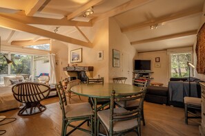 A spacious living area with a round table, multiple chairs, a sofa, and a television. - Between the ocean and the Bassin, near the tip, house with large garden (Lège-Cap-Ferret)