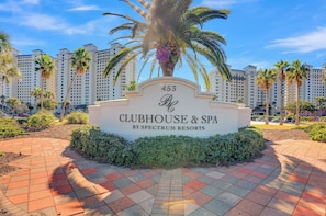 A sign for '453 Clubhouse & Spa by Spectrum Resorts' with a palm tree and a paved walkway. - The Beach Club 1401C by Liquid Life (Gulf Shores)
