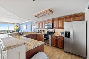 A modern kitchen with granite countertops, stainless steel appliances, and wooden cabinetry. - The Beach Club 1401C by Liquid Life (Gulf Shores)