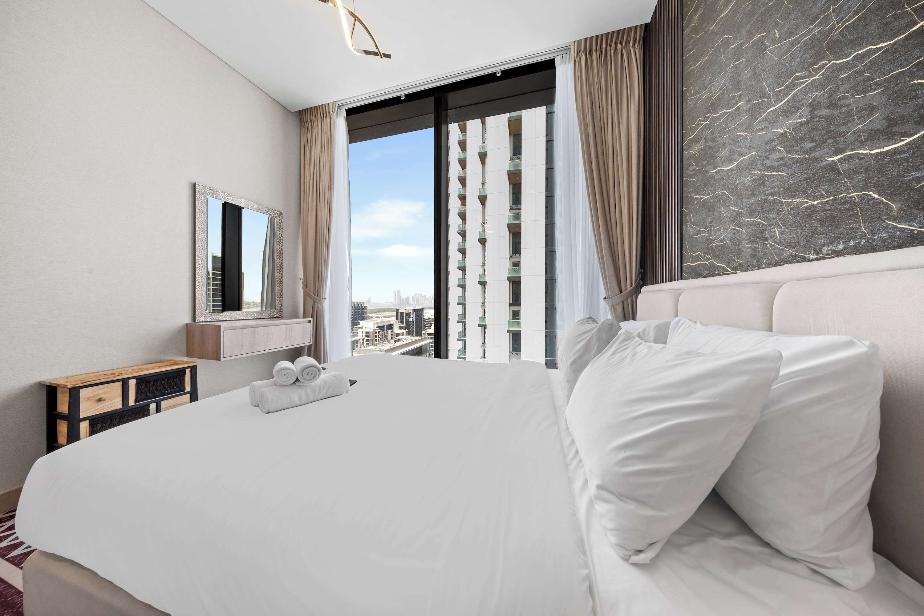 Ein Hotelzimmer mit einem grossen Bett, Blick auf die Stadt, einer Marmorwand und einer modernen Leuchte.