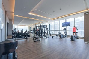 Ein großzügiger Fitnessraum mit unterschiedlichen Trainingsgeräten, großen Fenstern und einem Fernsehbildschirm.