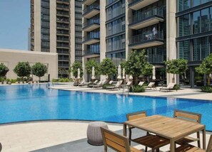Ein moderner Hotelpoolbereich mit einem klaren blauen Pool, Liegestühlen und einem Holztisch.