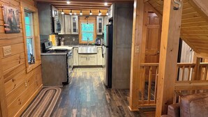 A wooden cabin interior with a kitchen, wooden walls, and a rug.
