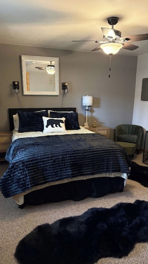 A bedroom with a bed, a ceiling fan, a nightstand, a lamp, and a chair. - The Cozy Wabasha Cabin (Wabasha)