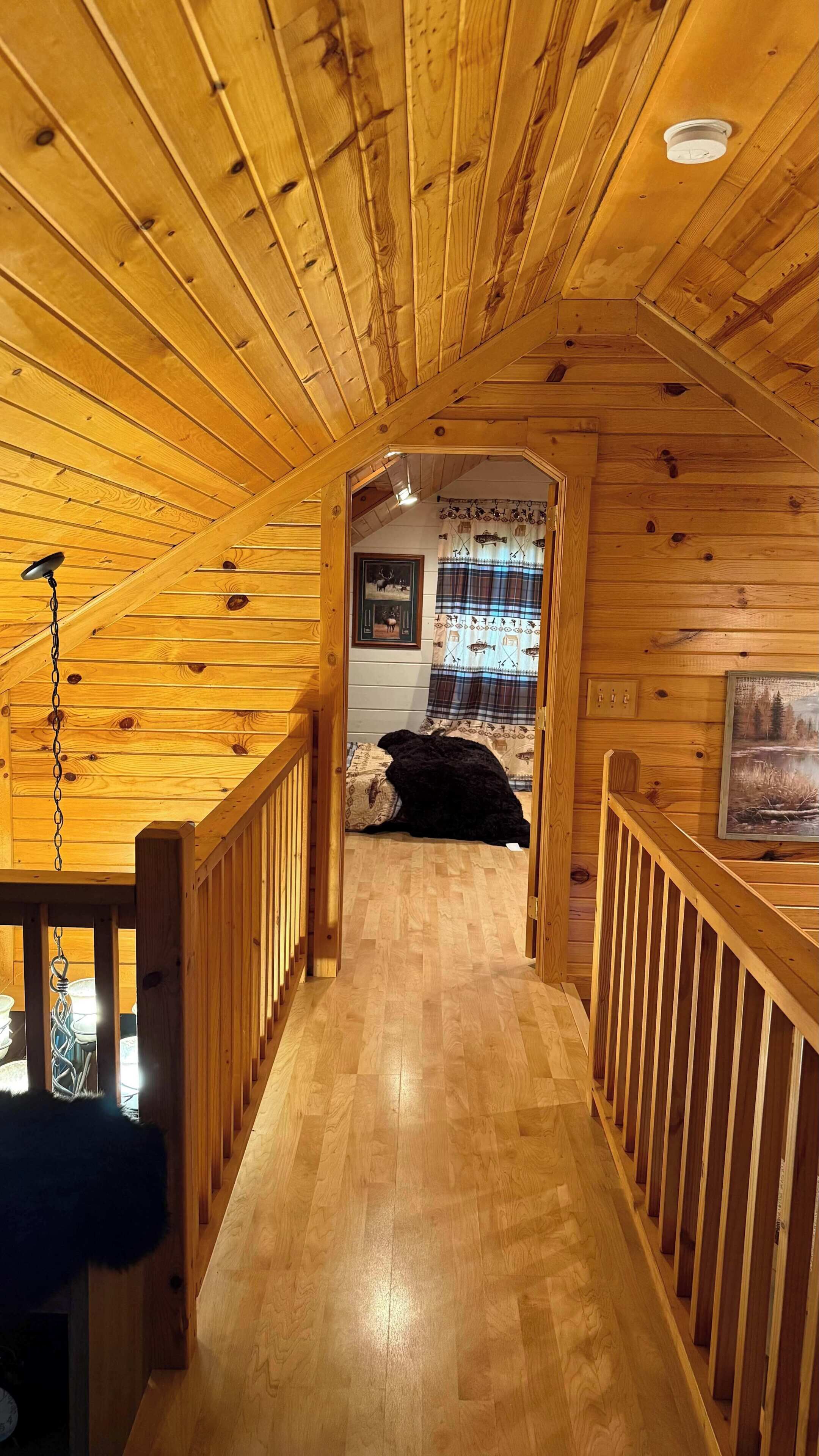 A wooden interior with a wooden floor, a staircase, and a bed with a blanket.