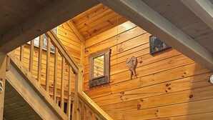 A wooden interior with a staircase, a cushioned bench, and a fireplace.