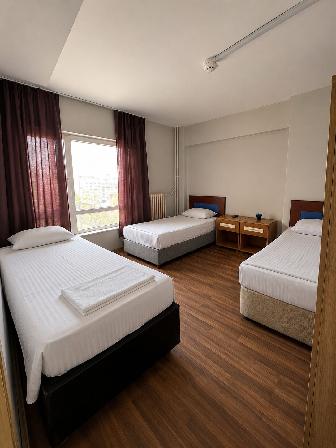A hotel room with two single beds, a desk, a chair, a radiator, and a window with curtains.