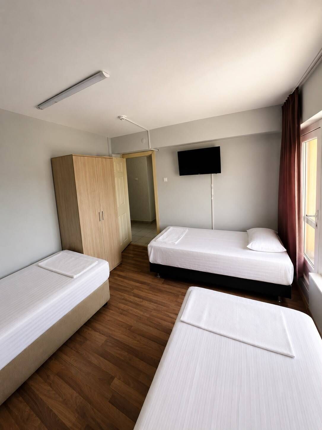 Una habitación con dos camas individuales, un armario, televisión y ventana con cortinas.