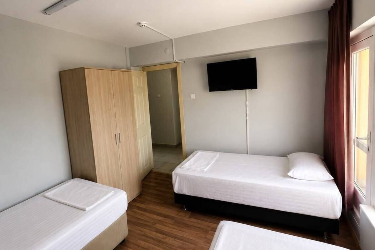 A room with two single beds, a wardrobe, a television, and a window with curtains.