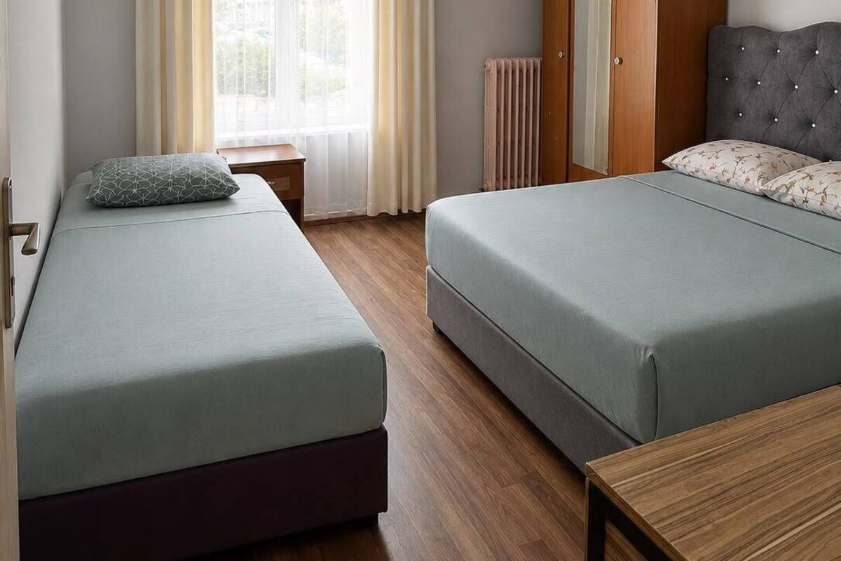 A hotel room with two beds, a wardrobe, a radiator, and a television.
