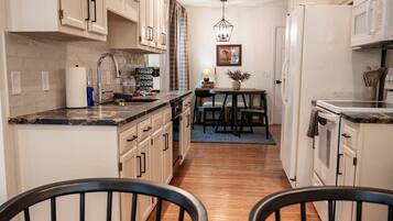 A modern kitchen with white cabinets, a dining area with a table and chairs, and a hanging light fixture.