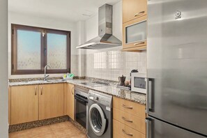 Eine Küche mit einem Edelstahl-Kühlschrank, einem eingebauten Backofen, einer Waschmaschine und einem Fenster mit Milchglas.