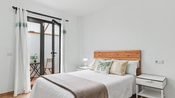 Een slaapkamer met een bed, nachtkastje en een schuifdeur naar een balkon.