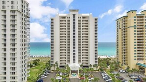 A high-rise hotel with a central courtyard, multiple balconies, and a view of the ocean.