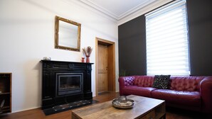 A living room with a fireplace, a red leather sofa, a wooden coffee table, and a large window with blinds.