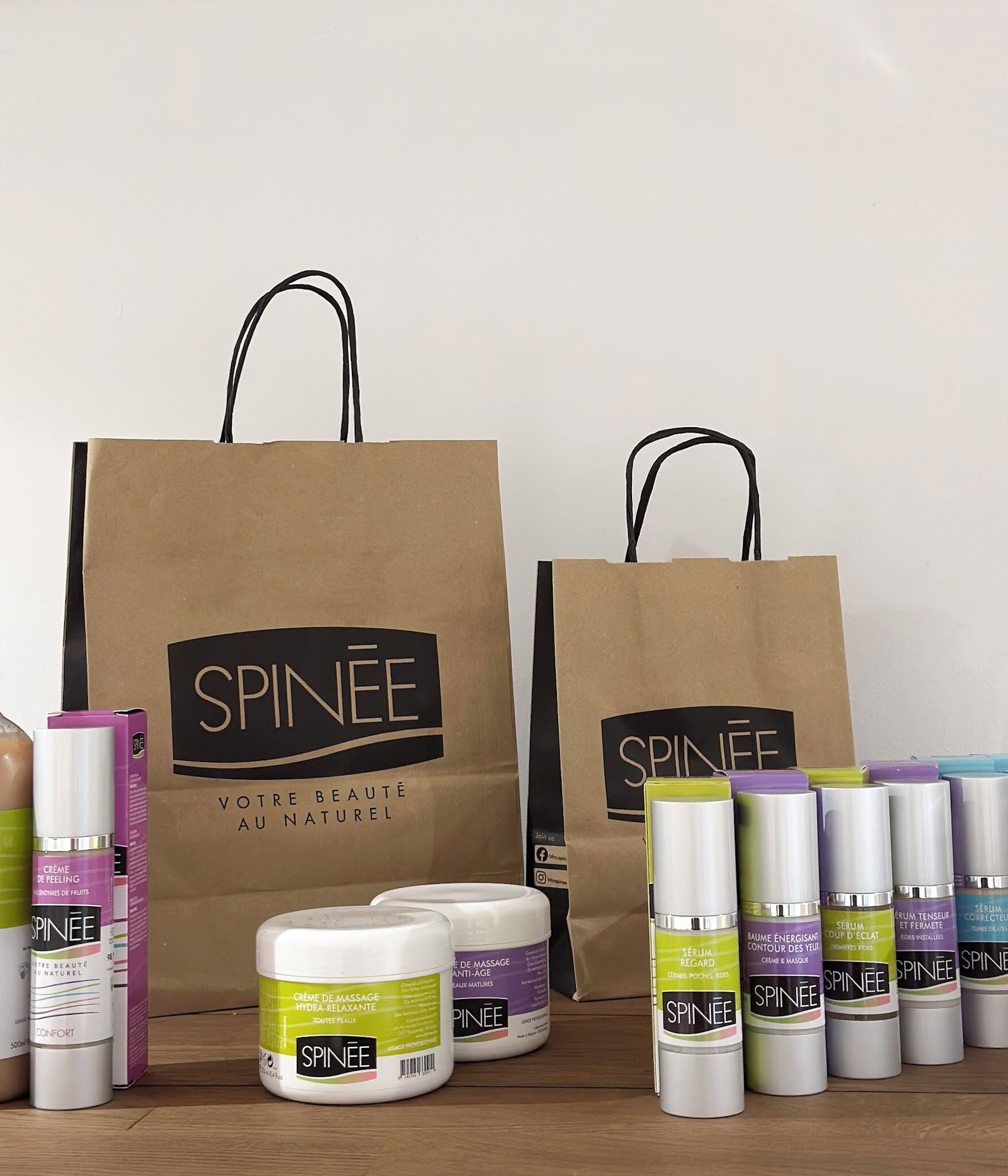 Dos bolsas de papel marrón con la marca 'SPINEE', varios productos para el cuidado de la piel y una superficie de madera.