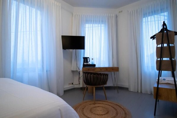 Et hotelværelse med seng, skrivebord med stol, fjernsyn og et vindue med let gardin.