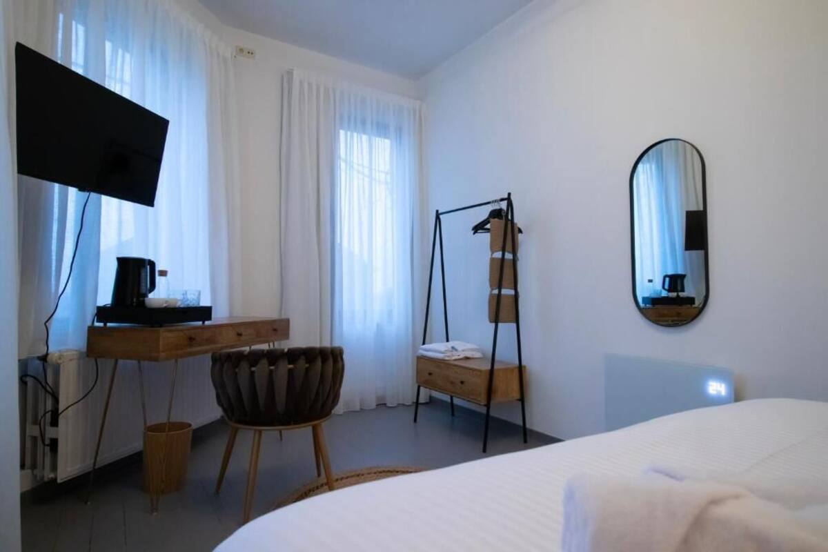Une chambre à coucher comprenant un lit, un bureau avec un téléviseur à écran plat, une chaise, un fauteuil suspendu, un miroir et une fenêtre avec des rideaux.