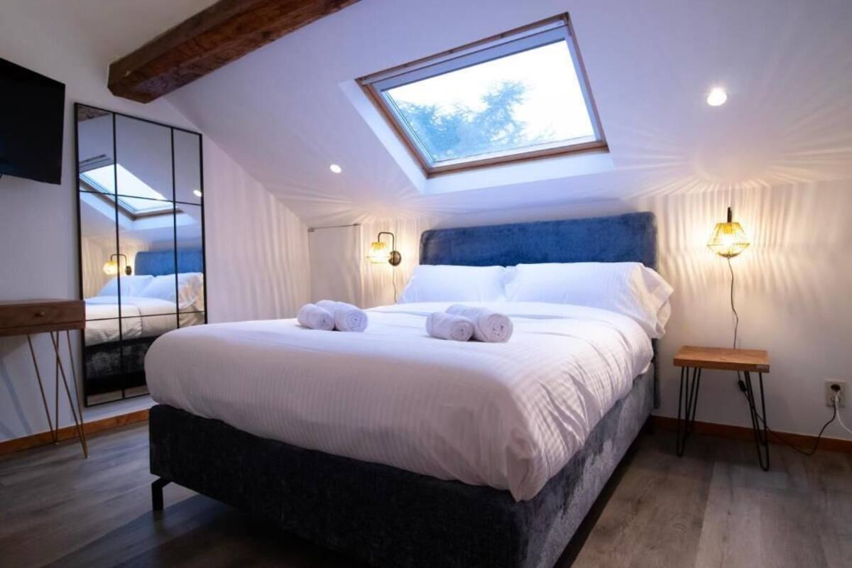Une chambre avec un puits de lumière, un lit avec du linge de lit blanc, une table de chevet et un téléviseur fixé au mur.