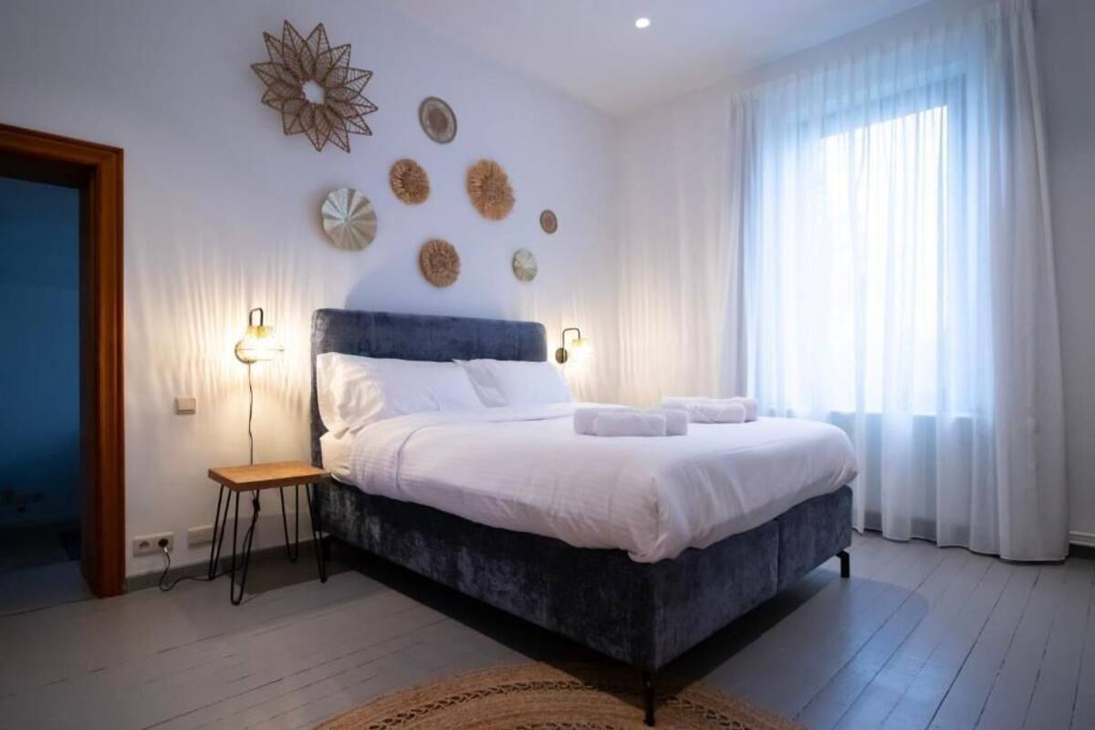 Une chambre à coucher avec un lit, des lampes de chevet, une petite table et des œuvres d’art décoratives au mur.