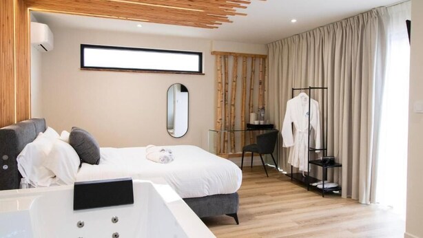 A modern hotel room with a bed, bedside table, mirror, and a clothing rack.