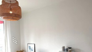 Ein modernes, minimalistisches Zimmer mit weißem Schreibtisch, Fernseher, Mikrowelle und einer Weidenhängeleuchte.