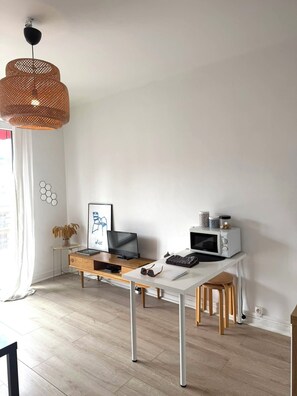 Ein modernes, minimalistisches Zimmer mit weißem Schreibtisch, Fernseher, Mikrowelle und einer Weidenhängeleuchte.