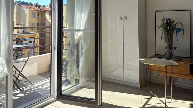 Ein Zimmer mit einer Schiebetür zum Balkon, einem weißen Kleiderschrank und einem kleinen Tisch mit einer Vase.