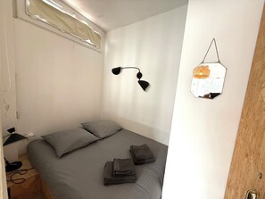 Ein Schlafzimmer mit einem Bett, einer Wandlampe, einem Spiegel und einer Holztür.