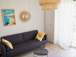 Ein modernes Wohnzimmer mit einem grauen Sofa, einem runden Spiegel, einer Korbtasche als Lampe und einem gerahmten Bild an der Wand.