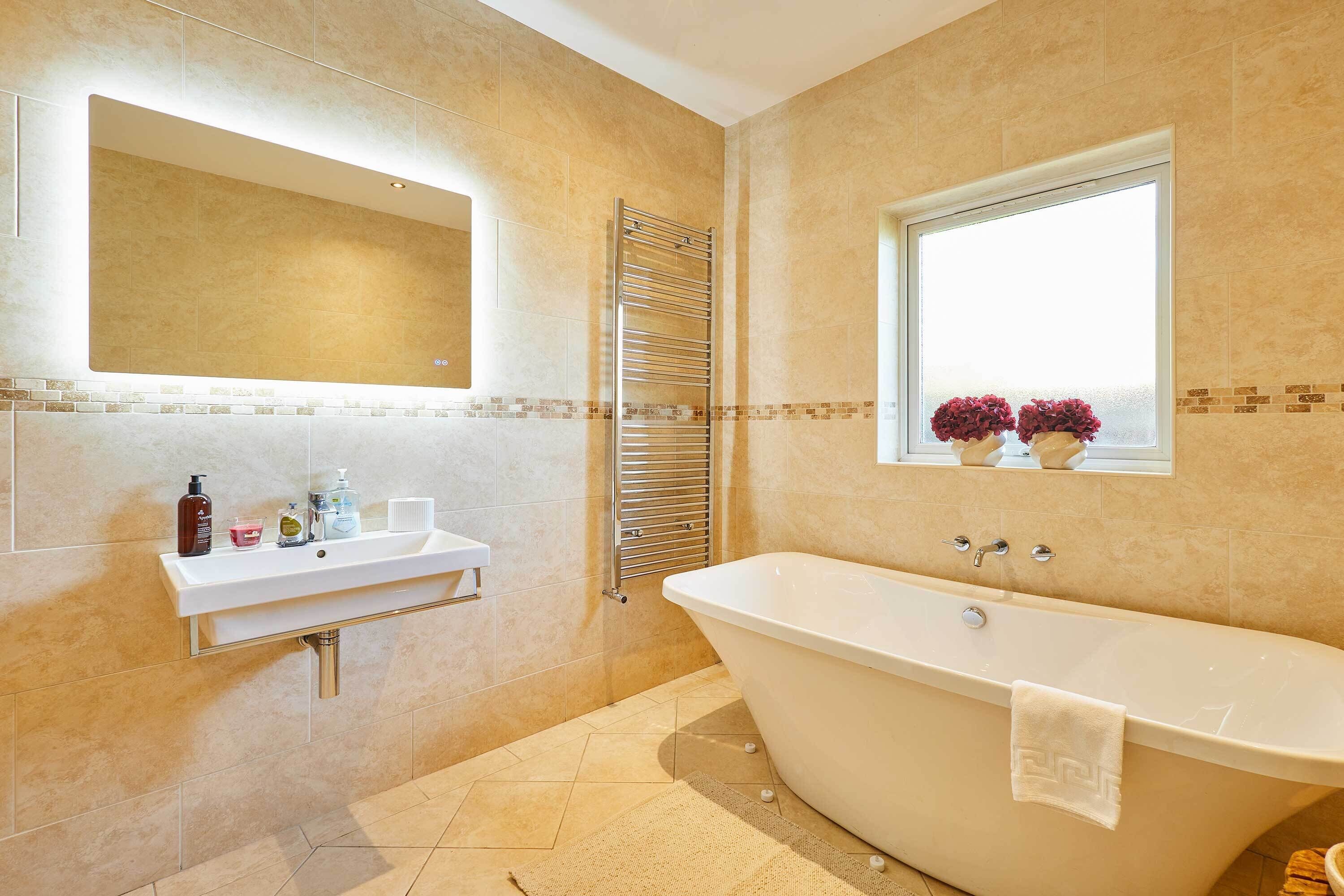 Une salle de bain avec une baignoire sur pieds, un lavabo avec un miroir au-dessus et une fenêtre ornée de fleurs.