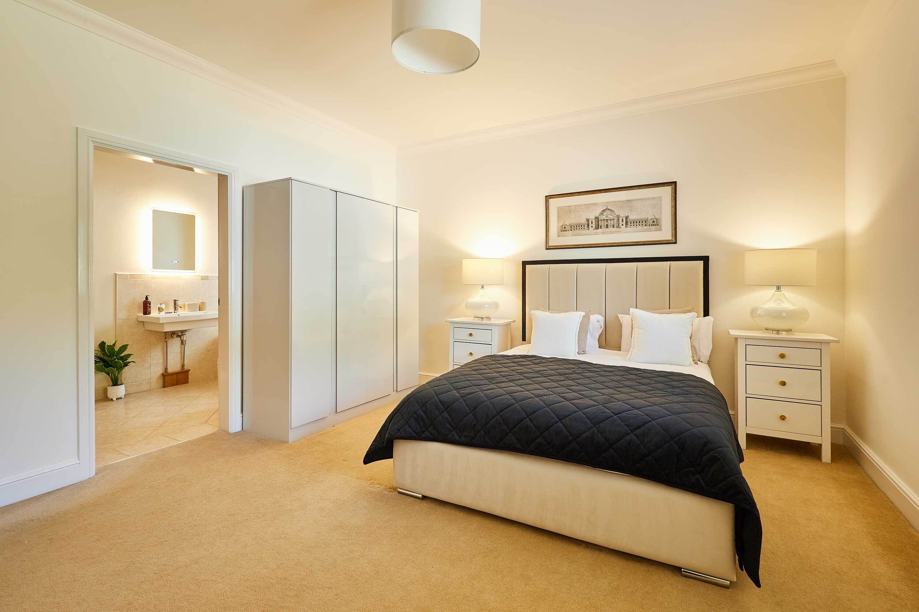 A bedroom with a bed, bedside tables, a nightstand, a mirror, and a framed picture on the wall.