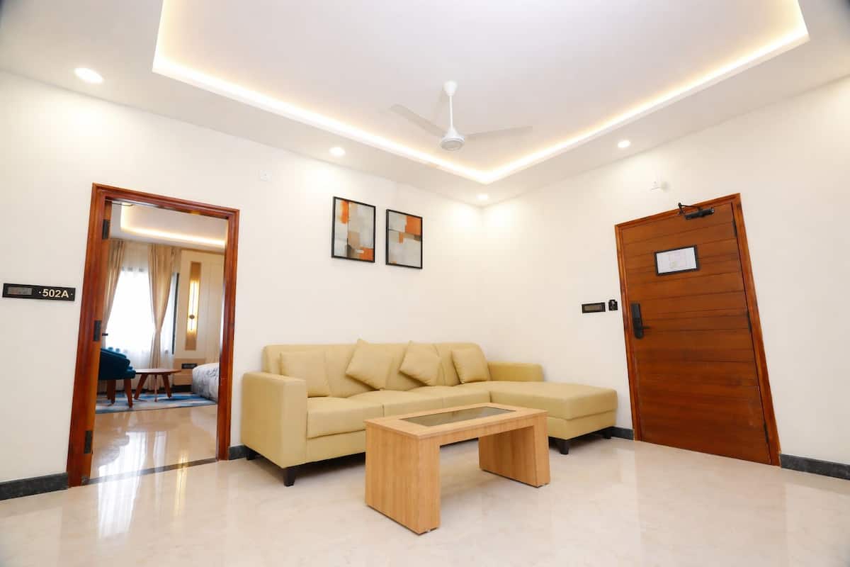A modern hotel room with a beige sofa, a wooden coffee table, a ceiling fan, and a door with a sign.